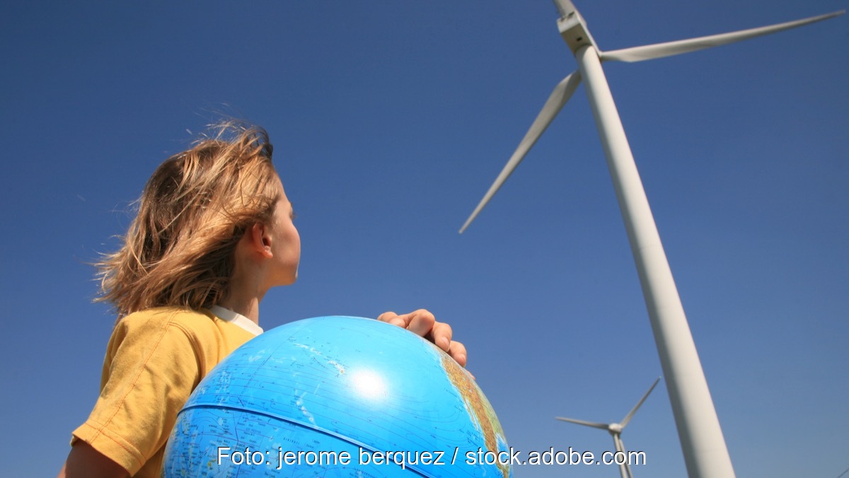 Ein Kind mit einer Weltkugel neben Windkraftanlagen, als Symbol für Energieerzeugung, erneuerbare Energien, Kohleausstieg