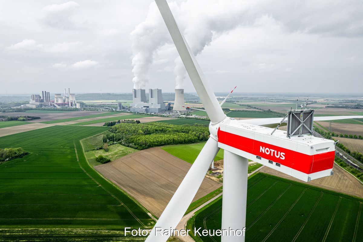 Luftaufnahme zeigt eine Windenergieanlage vor Braunkohlekraftwerk im Hintergrund.